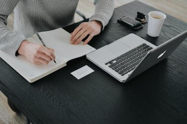 Open notebook with a pen and a cup of coffee on a wooden table